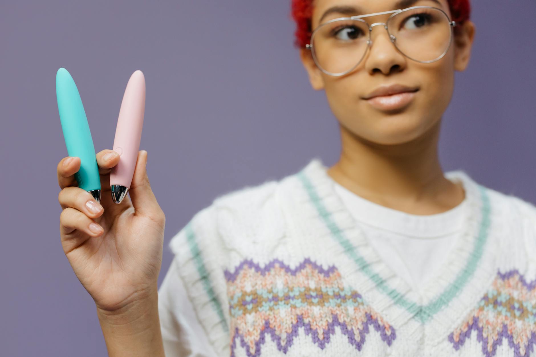 A person holding two vibrators against a purple background, symbolizing intimate pleasure exploration