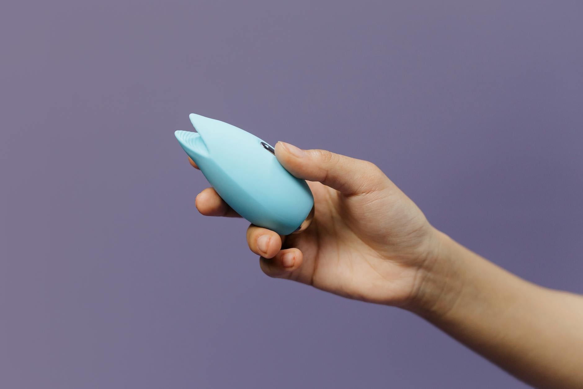 Blue silicone clitoral vibrator held gently in hand, representing pleasure recovery after injury
