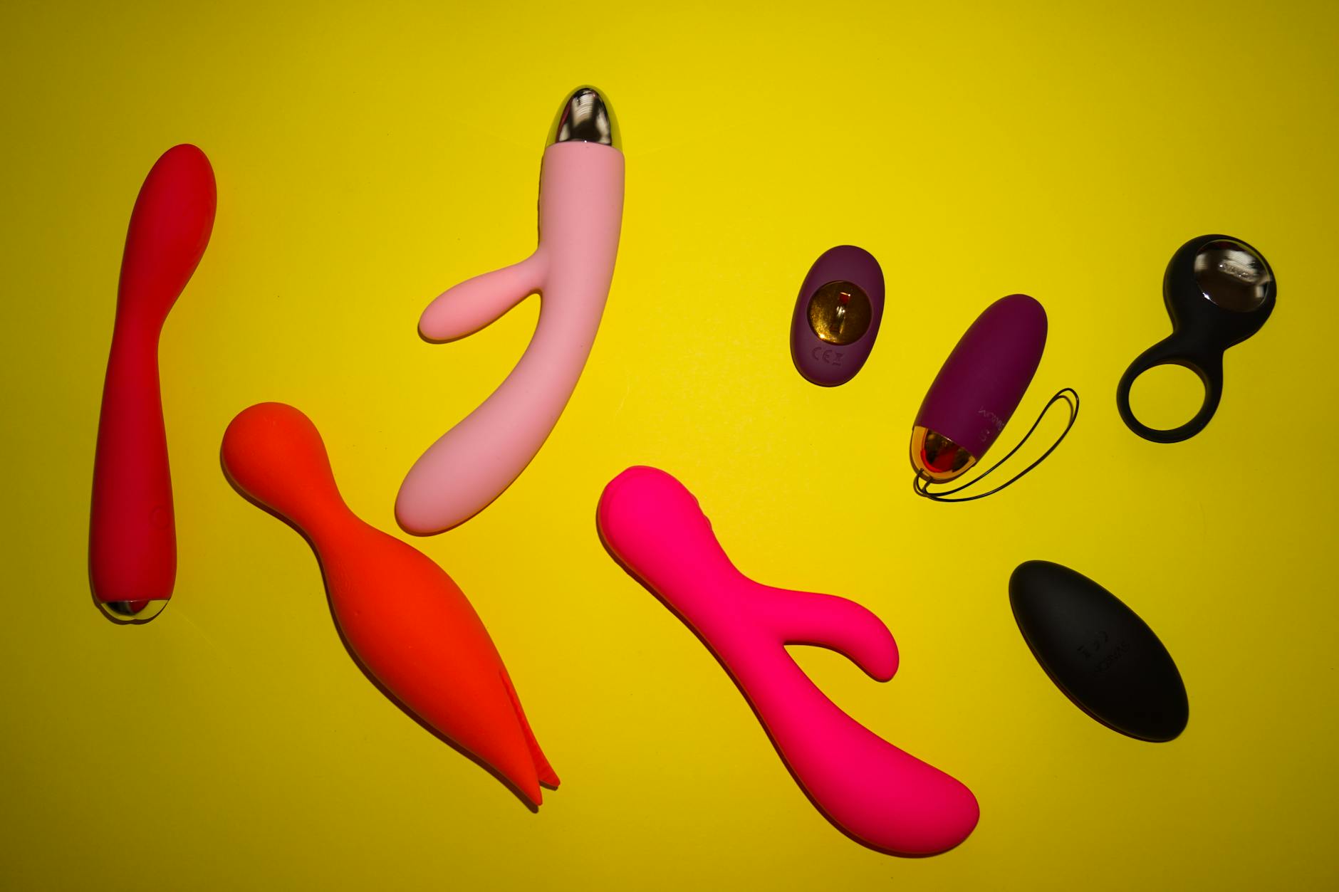 Deux mains examinant une collection de jouets érotiques colorés sur une table blanche