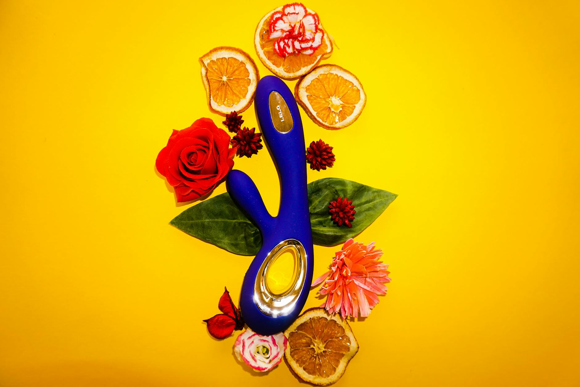 Blue vibrator surrounded by fresh lemons and flowers on a bright yellow background